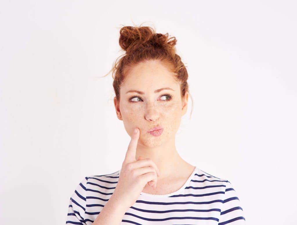 Woman with red hair wearing a black and white stripped shirt thinking.