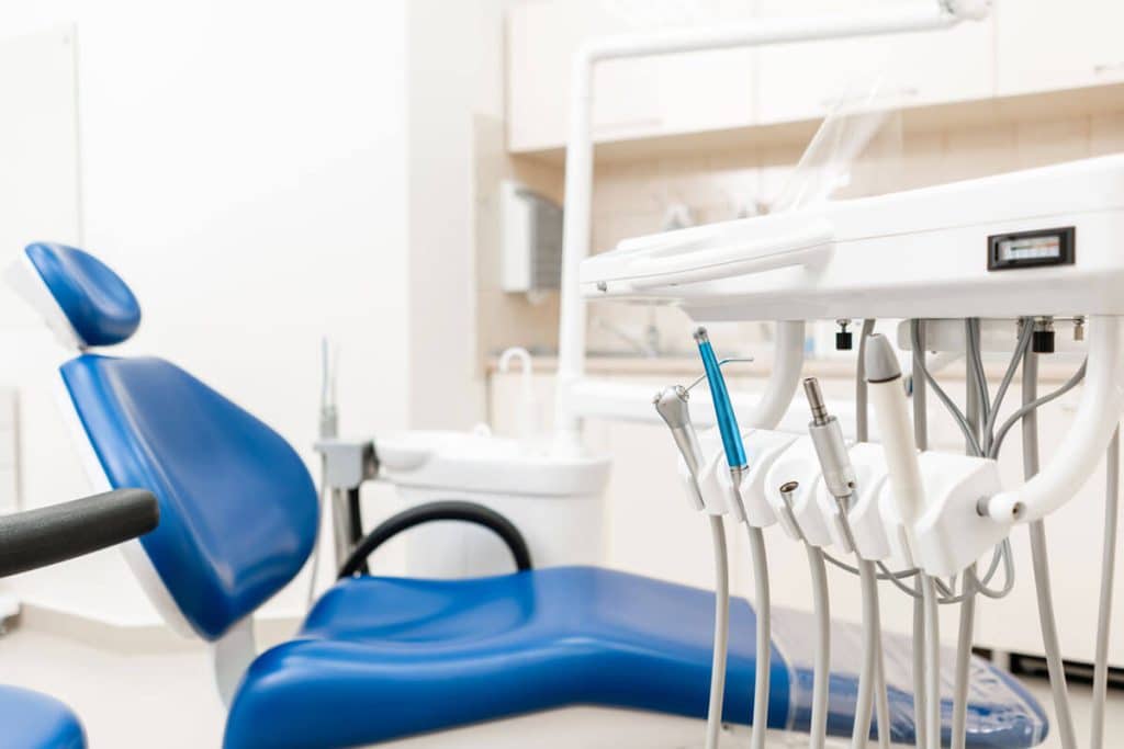 Blue dental exam chair in white room with several dental tools