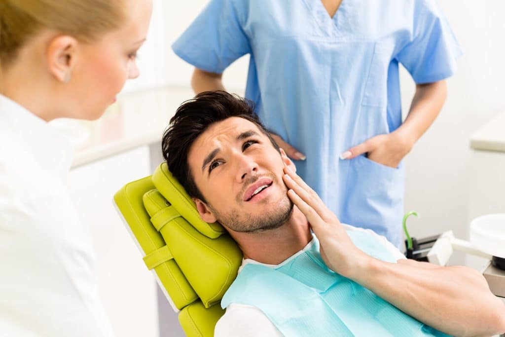 a man in a dental chair holds his jaw