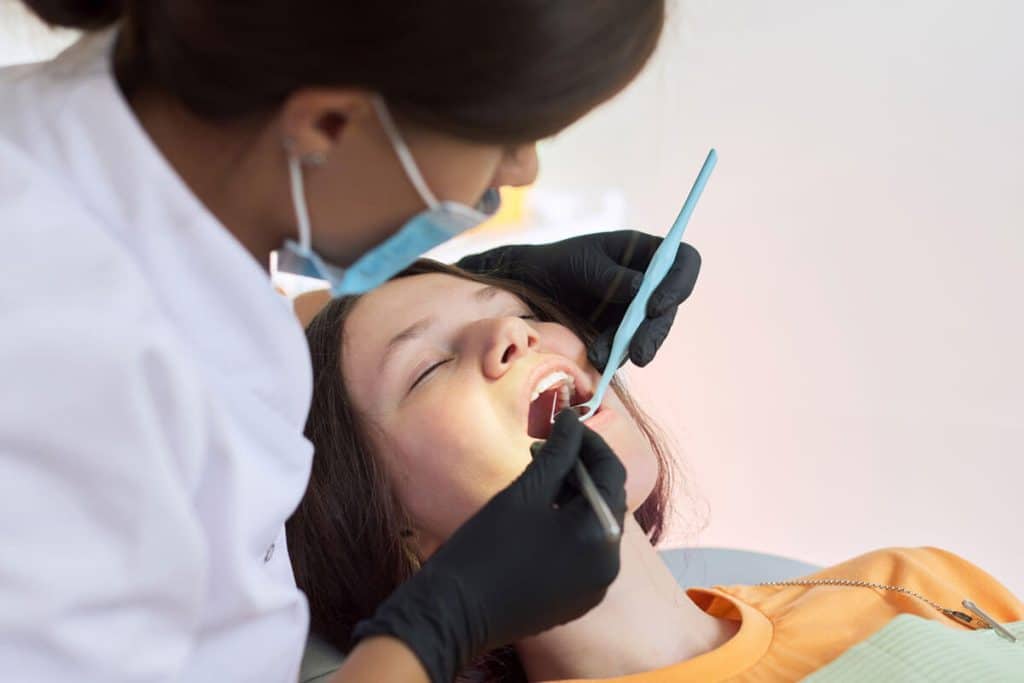 Female dentist examining female patient's teeth with dental tools