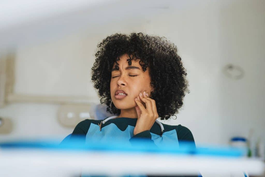 a woman holds her jaw and grimaces